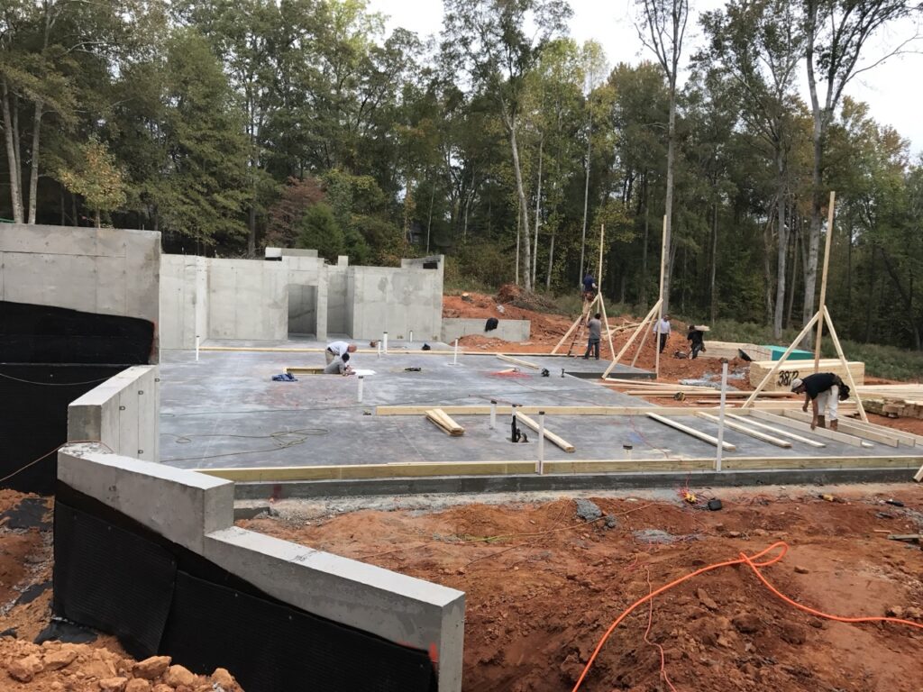 Freshly poured concrete foundation on a cleared land plot, showcasing the initial phase of constructing a new home, with visible foundation forms and surrounding natural landscape.