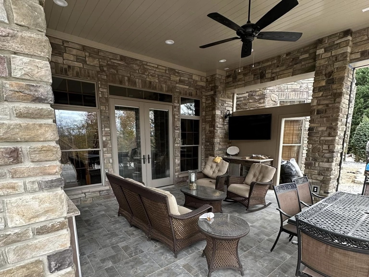 Covered stone patio with wicker seating and an outdoor television mounted on the wall