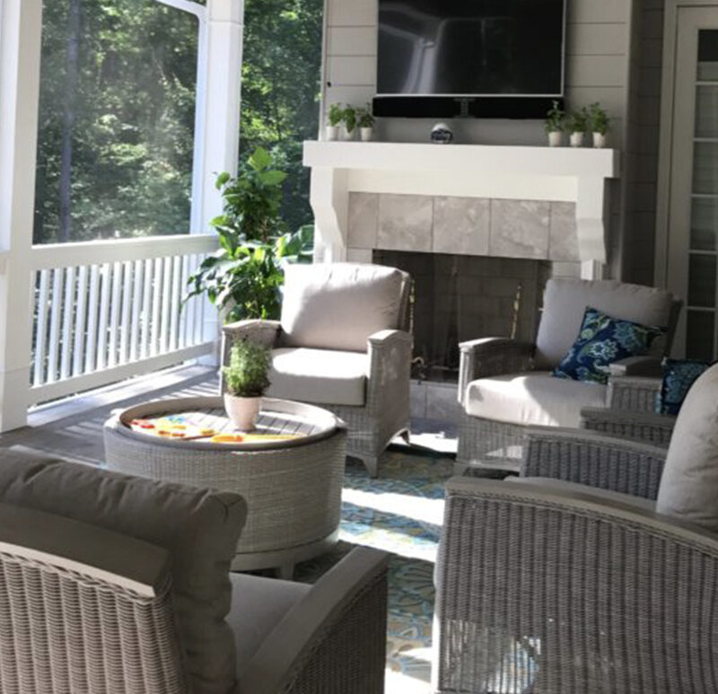 Screened-in porch with wicker chairs, sofa, round wicker coffee table, and stone fireplace.