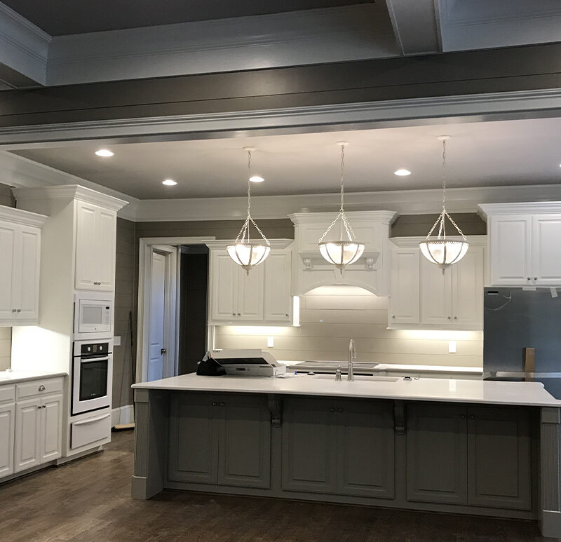Spacious kitchen with white cabinetry, gray island, pendant lights, and dark ceiling beams.
